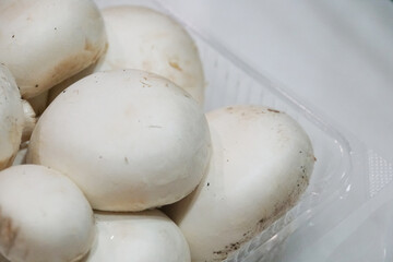 Close up of the cap of white button mushrooms, in a plastic tray.