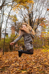 cute brunette teen girl in gray coat jumps in the autumly forest . Cosiness, autumn, fun