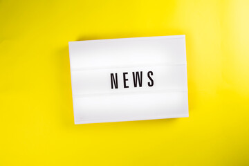 News word on lightbox on yellow background isolated. Top view, flat lay. world imbued with information, informational reasons, daily news, messages, informational noise concept