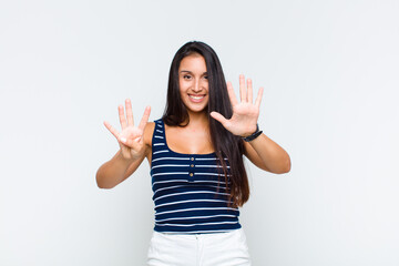 young woman smiling and looking friendly, showing number nine or ninth with hand forward, counting...