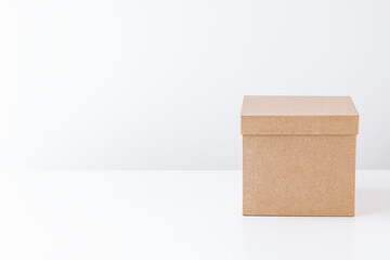 Closed cardboard box on a white table on the back of a white wall. Gift concept. Place for text.