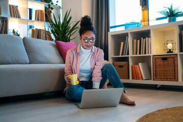 Attractive happy young entrepreneur woman working with laptop while drinking a cup of coffee...