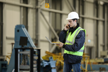 Portrait of a man , factory engineer in work clothes holding laptop and phone, controlling the work process at the helicopter manufacturer.