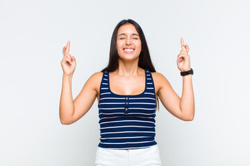 young woman smiling and anxiously crossing both fingers, feeling worried and wishing or hoping for...