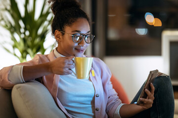 Happiness young entrepreneur woman using her smart phone while drinking a cup of coffee sitting on couch in the office.