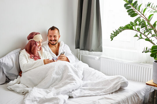relaxed couple use mobile phone lying on bed together, caucasian man and woman happy to have rest, look at screen of mobile phone