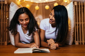 Young latin mother and her daughter reading book at home