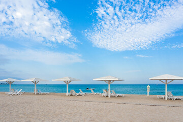 View of the sandy seashore with white beach umbrellas and rare vacationers. Shooting from the air.