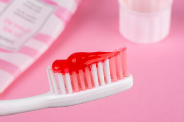 Pink toothbrush and pink toothpaste on a pink background.