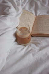 Close up of iced coffee with ice cubes on it. White sheet accompanied by an open book. Minimalist aesthetic photography detail. Product Photography 2020. 