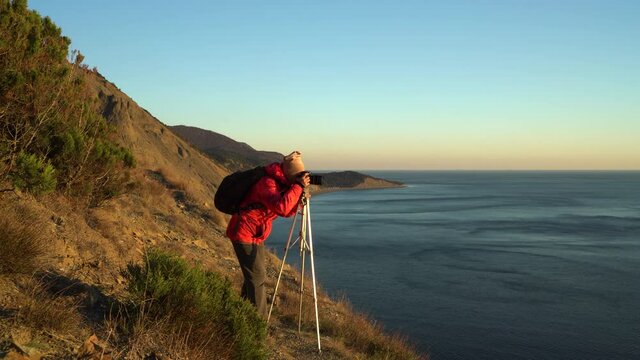 
female photographer takes pictures with a tripod at sunset in the highlands on the coast. Mountains on the Black Sea coast.