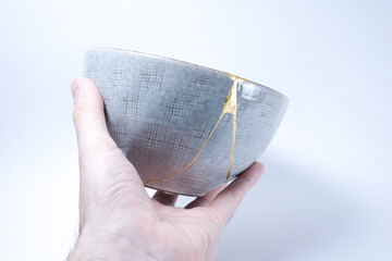 Hand holding kintsugi bowl. Gold cracks restoration on pottery restored with the antique Kintsugi...