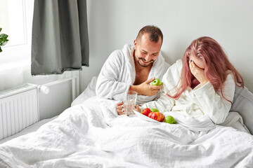 Obraz na płótnie Canvas happy couple enjoy breakfast on bed, they laugh while eating fresh apples, joyful time in the morning, at home. love concept
