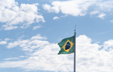 Brazilian flag flying and in the background the blue sky with white clouds