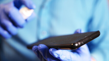 Hand in protective glove with alcohol spray cleaning mobile phone. Covid-19 disinfection concept.