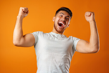 Portrait of excited, successful man raising hands up