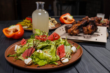 Caesar salad with grapefruit with grilled pork ribs, pickled vegetables and moonshine  on black wooden background