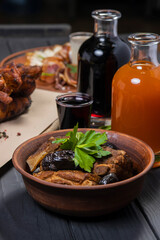 Stewed ribs with prunes in a plate, with wine on black wooden background