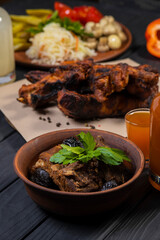 Stewed ribs with prunes in a plate, with wine on black wooden background