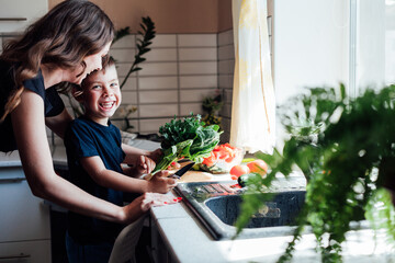Mom and young son cut vegetables for salad in the kitchen