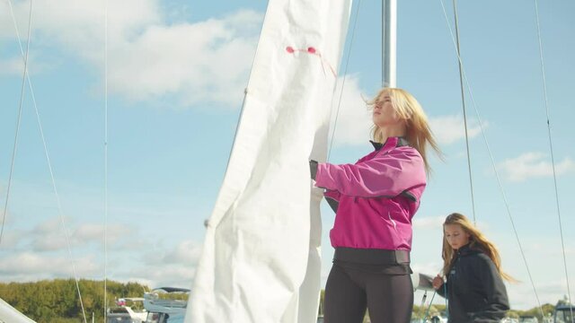 The women's yacht team in the dock jointly puts the mainsail on the mast of a white sports yacht for the North sea regatta.