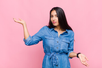 young woman shrugging with a dumb, crazy, confused, puzzled expression, feeling annoyed and clueless