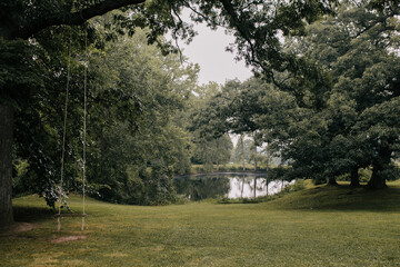 Obraz premium Wooden swing in garden with pond on rainy day