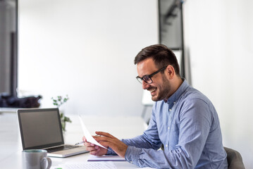 Young smiling cheerful confident businessman entrepreneur checking working plan schedule or timetable business deal document agreement in office copy space screen empty modern bright office