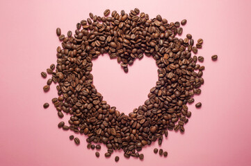 heart shaped coffee made of coffee beans on a pink background