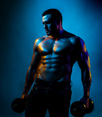 Shirtless sexy bodybuilder is doing exercise with dumbbell. Neon blue light.