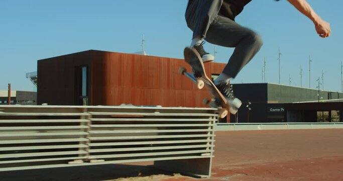 Young cool millennial man, teenager hipster in California rides his skateboard on boardwalk beach. Action wide shot of man perform skateboard tricks on sunny day in tourist spot over bench