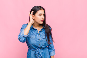 young woman looking serious and curious, listening, trying to hear a secret conversation or gossip,...