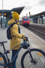 Vertical photo of a man in winter clothes, waiting with his bike, the train. In the background the...