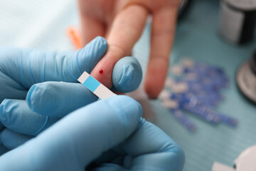Doctor holding test strip near patients finger with drop of blood in clinic closeup. Glucometry in diabetes mellitus concept