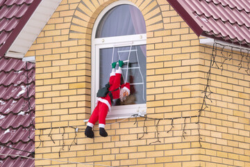 Santa Claus climbing up a wall into a window. Traditional Christmas decoration.