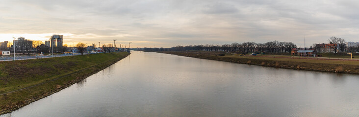 Cloudy panorama of Odra river between green coasts of city at sunset