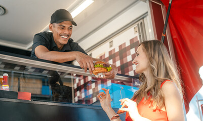 Cook in a food truck handing tasty burger over to woman customer