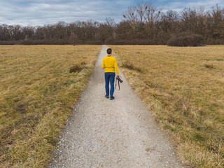 Fototapeta premium Man walk on Long path to forest between yellow fields at sunny morning