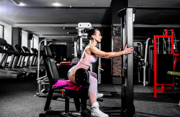 Naklejka na ściany i meble A girl in sportswear in a professional gym works out with fitness equipment. Healthy lifestyle concept