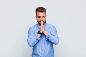 young man feeling worried, hopeful and religious, praying faithfully with palms pressed, begging...