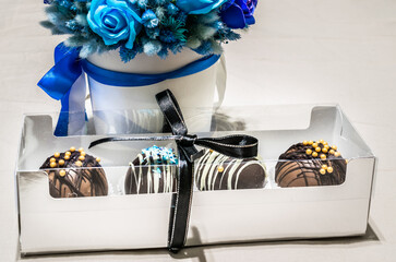 Set of chocolate bombs in giftbox with mini marshmallows, white chocolate, milk chocolate, hot cocoa, ingredients that melts with hot milk. Delicious winter holidays dessert with bouquet of blue roses