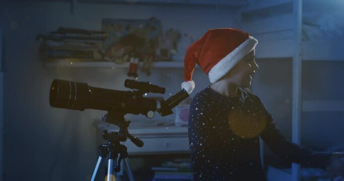Cinematic night shot of happy little girls sisters wearing starry pajamas and santa hats are watching through telescope with magic glows arrival of Santa Claus on Christmas day in the starry sky.