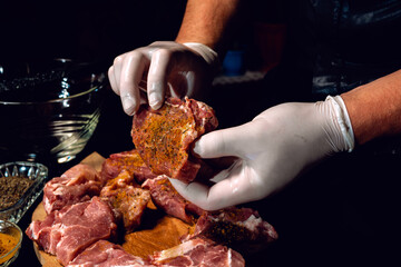 Marinating pork neck skewers, adding salt, curry and basil to the meat, pieces of meat on a wooden board.