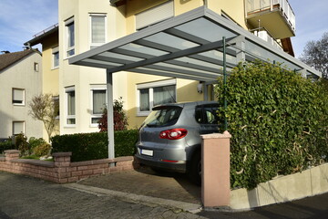 Neuer grauer Carport aus beschichtetem Aluminium mit Pult-Glasdach an einem Wohnhaus