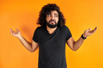 doubtful arab male is misunderstanding, show his incomprehension expression at camera, isolated over orange background - obrazy, fototapety, plakaty