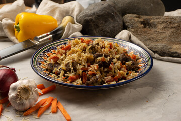 Hot pilaf with lamb or beef in a decorative national Uzbek plate with a traditional pattern. A classic oriental dish made of boiled rice, meat and vegetables with spicy spices.