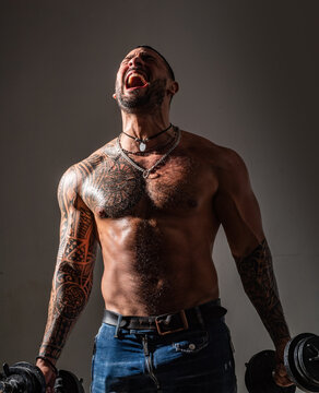 Screaming muscle man. Excited fit muscular guy exercising with dumbbell. Sporty hunk with naked torso. Strength and motivation.