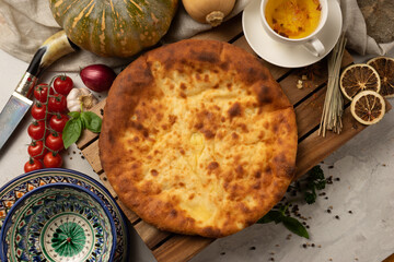Hot Ossetian pie with pumpkin filling and herbs next to decorative national Uzbek ceramic dishes with a traditional pattern. Classic oriental pastries for tea.