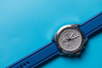 Reloj de pulsera plateado con correa azul sobre fondo azul cielo, con espacio para texto....