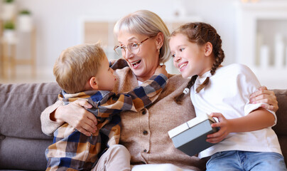 Excited grandmother hugging grandchildren with gift.